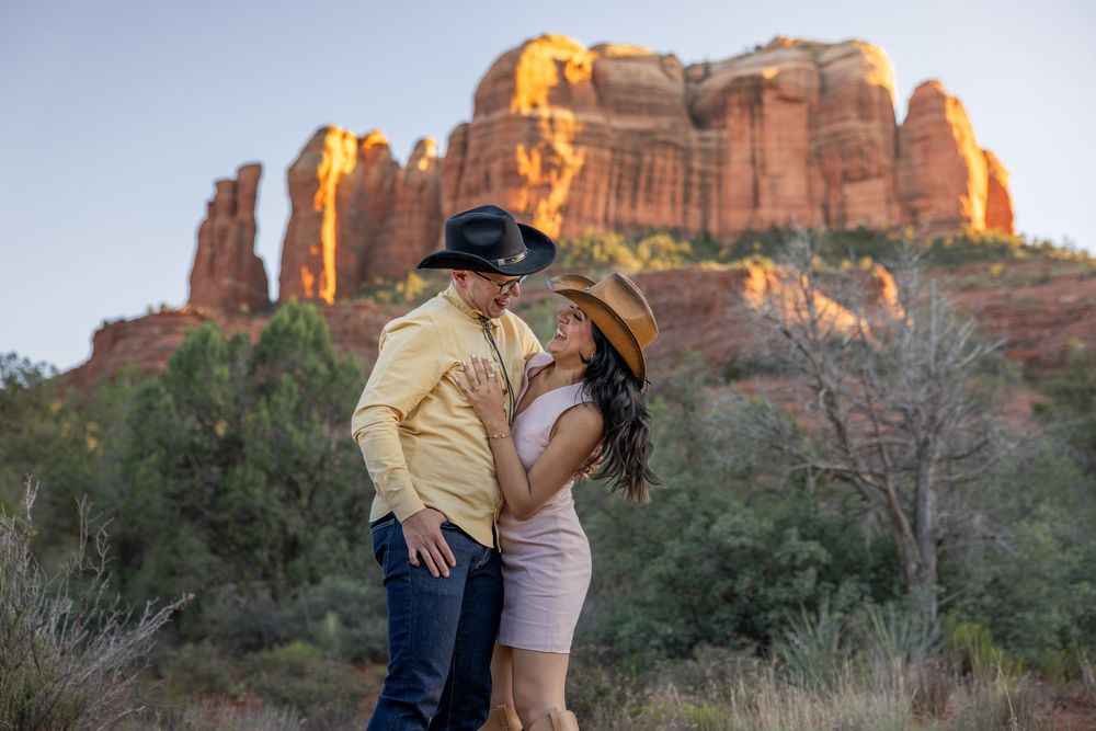 Couple sharing a romantic moment in cowboy hats with Cathedral Rock in Sedona at golden hour.