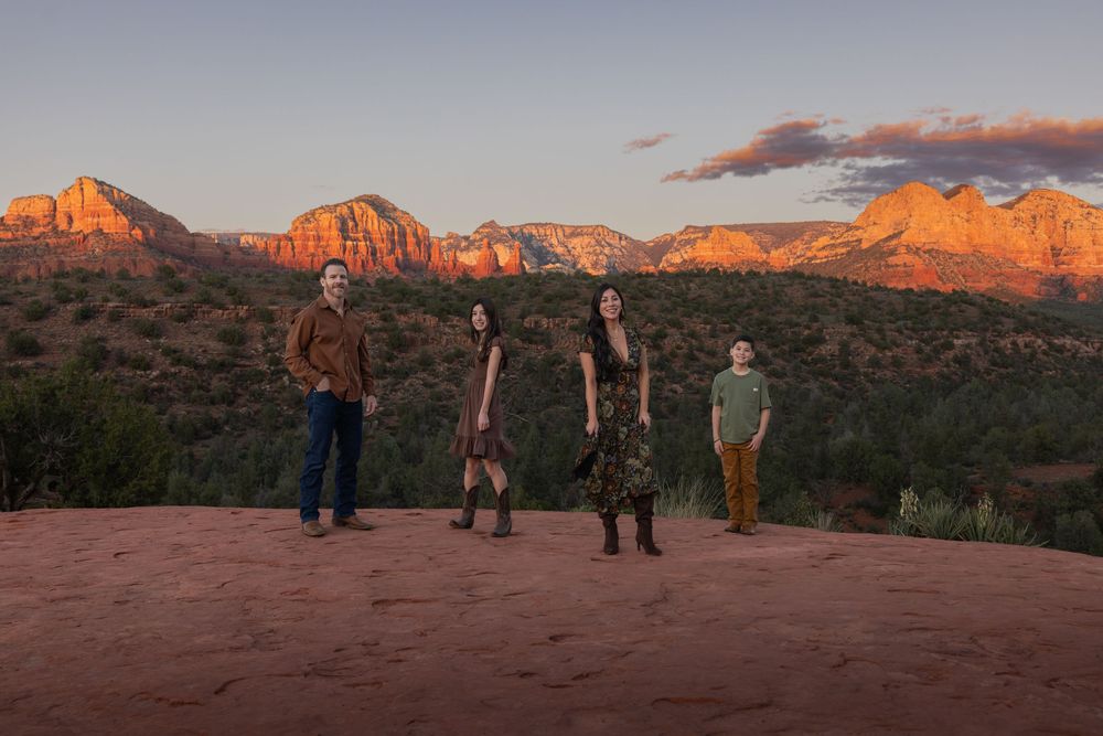 Family of four posing on red rock overlook with panoramic Sedona mountain views at sunset.