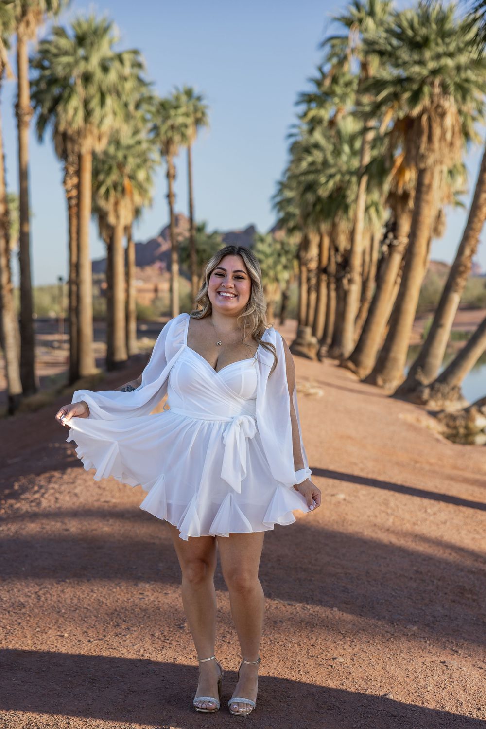 Woman in white mini dress twirling among palm trees on a sunny day in Arizona.