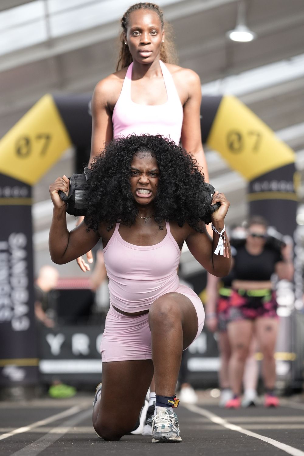 Hyrox athlete performing sandbag lunges with partner during race, showcasing strength, teamwork, and functional fitness competition.