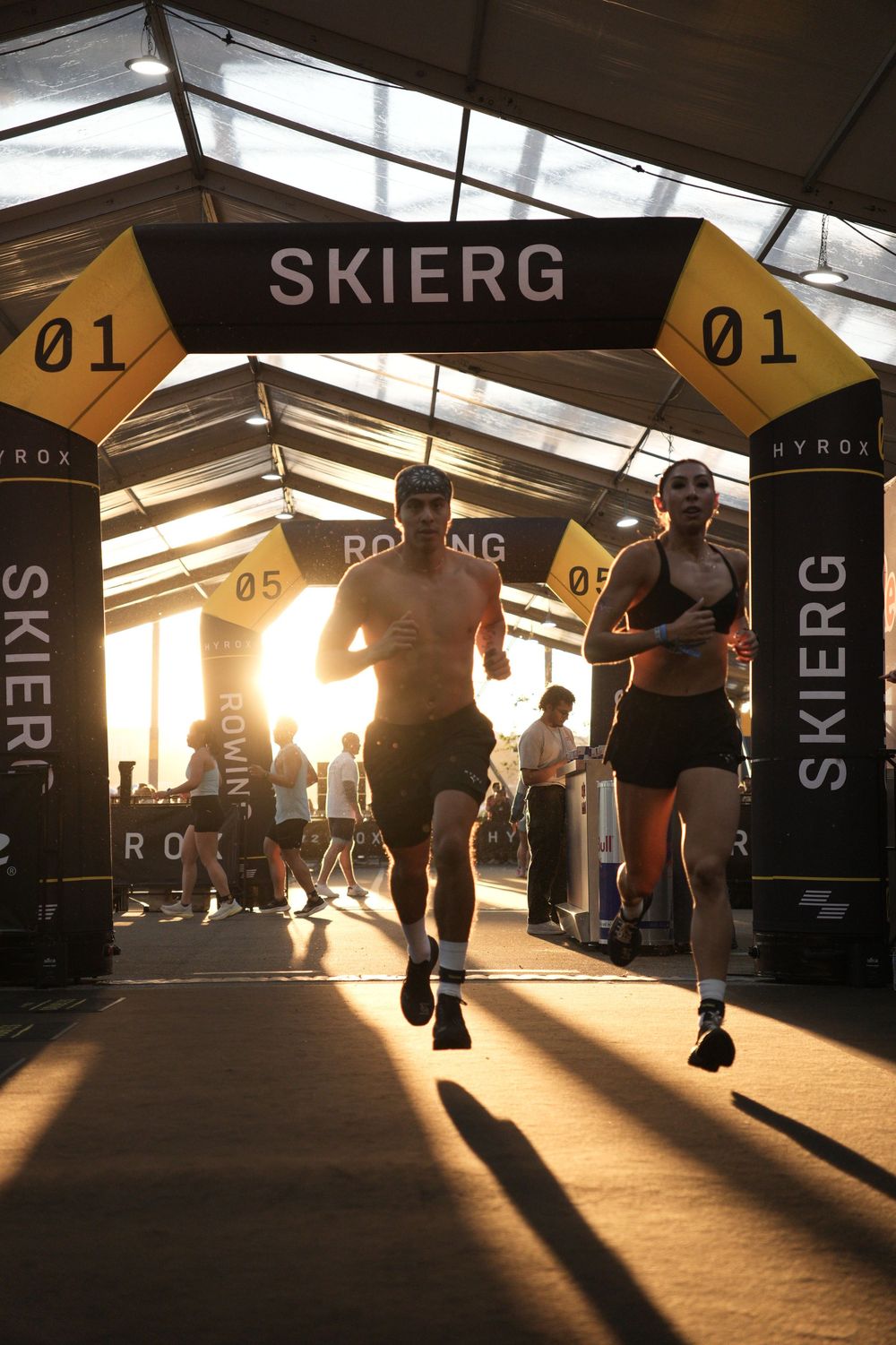 Hyrox athletes running toward the SkiErg station at sunset, capturing speed, endurance, and race atmosphere in fitness competition.
