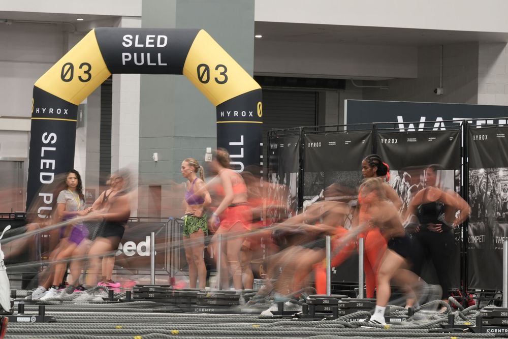 Long exposure photograph of athletes competing in the Hyrox sled pull station, emphasizing speed, movement, and the intensity of functional