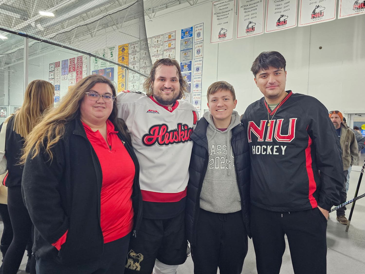 Four people smile together at an indoor ice hockey rink, two wearing NIU Huskies hockey jerseys.