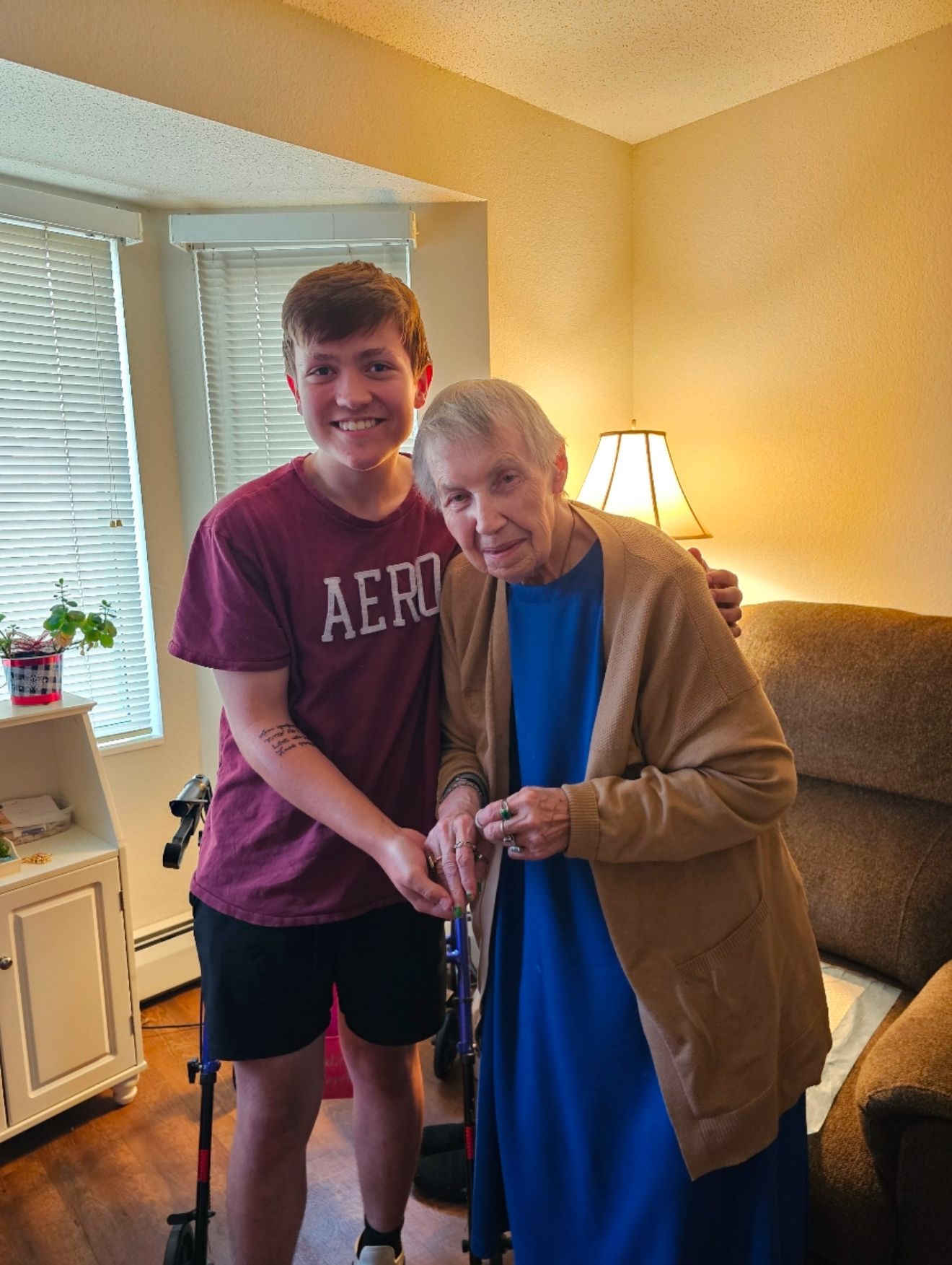 Young man in Aeropostale shirt poses with elderly woman using a walker in a cozy living room.