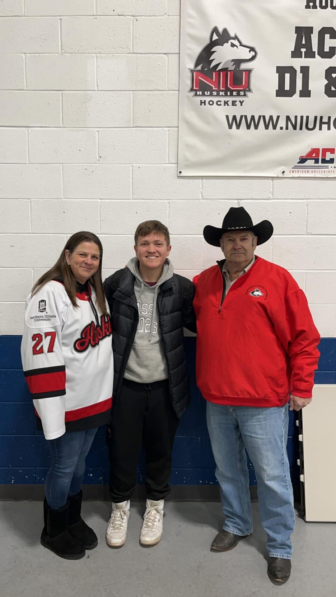 Three people posing together at NIU Huskies Hockey rink, wearing team jerseys and fan gear.