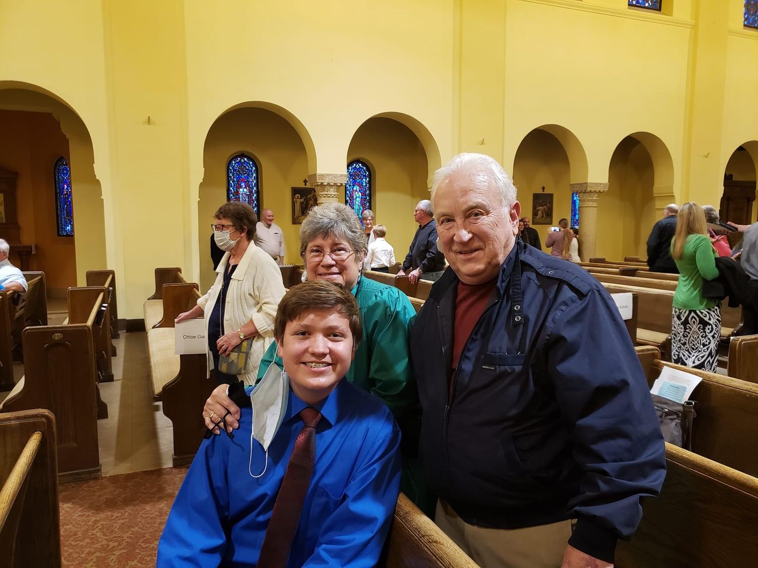 Family of three posing together in church pews, smiling for a photo during a religious ceremony or service.