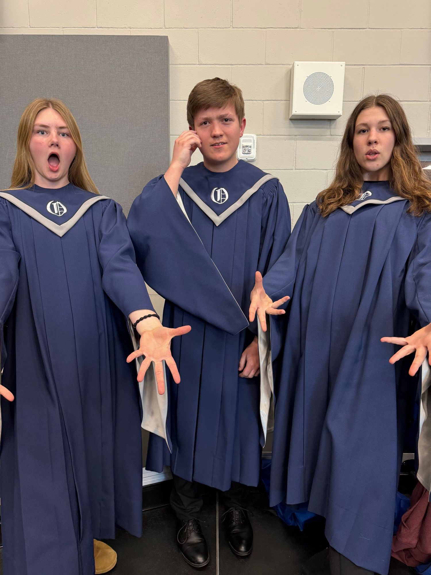Three students in blue choir robes posing dramatically backstage before a choral performance.
