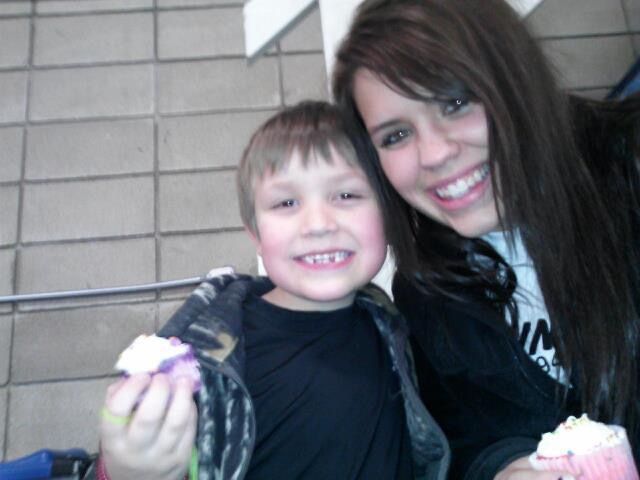 A smiling young boy and teenage girl posing together outdoors, both holding treats, enjoying a fun day out.