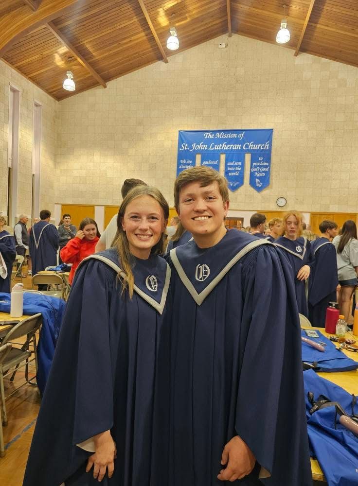Two students in navy blue graduation robes smiling at St. John Lutheran Church confirmation ceremony.