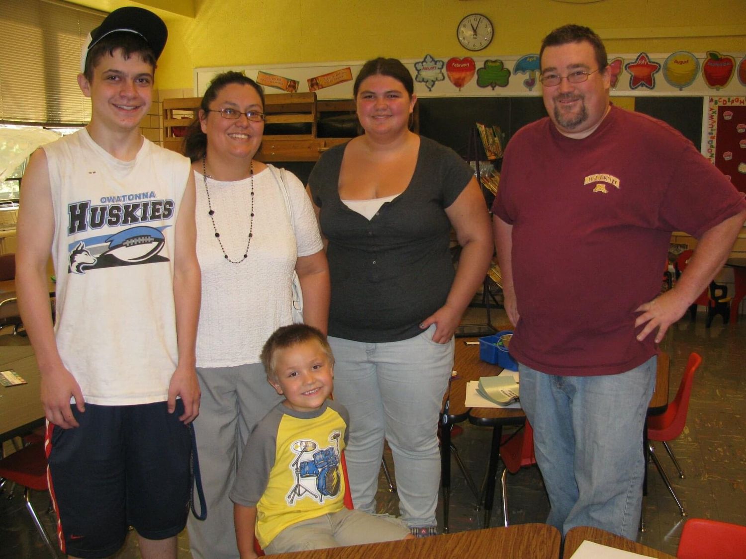 Family of five posing together in a colorful elementary school classroom, including three adults and two children.