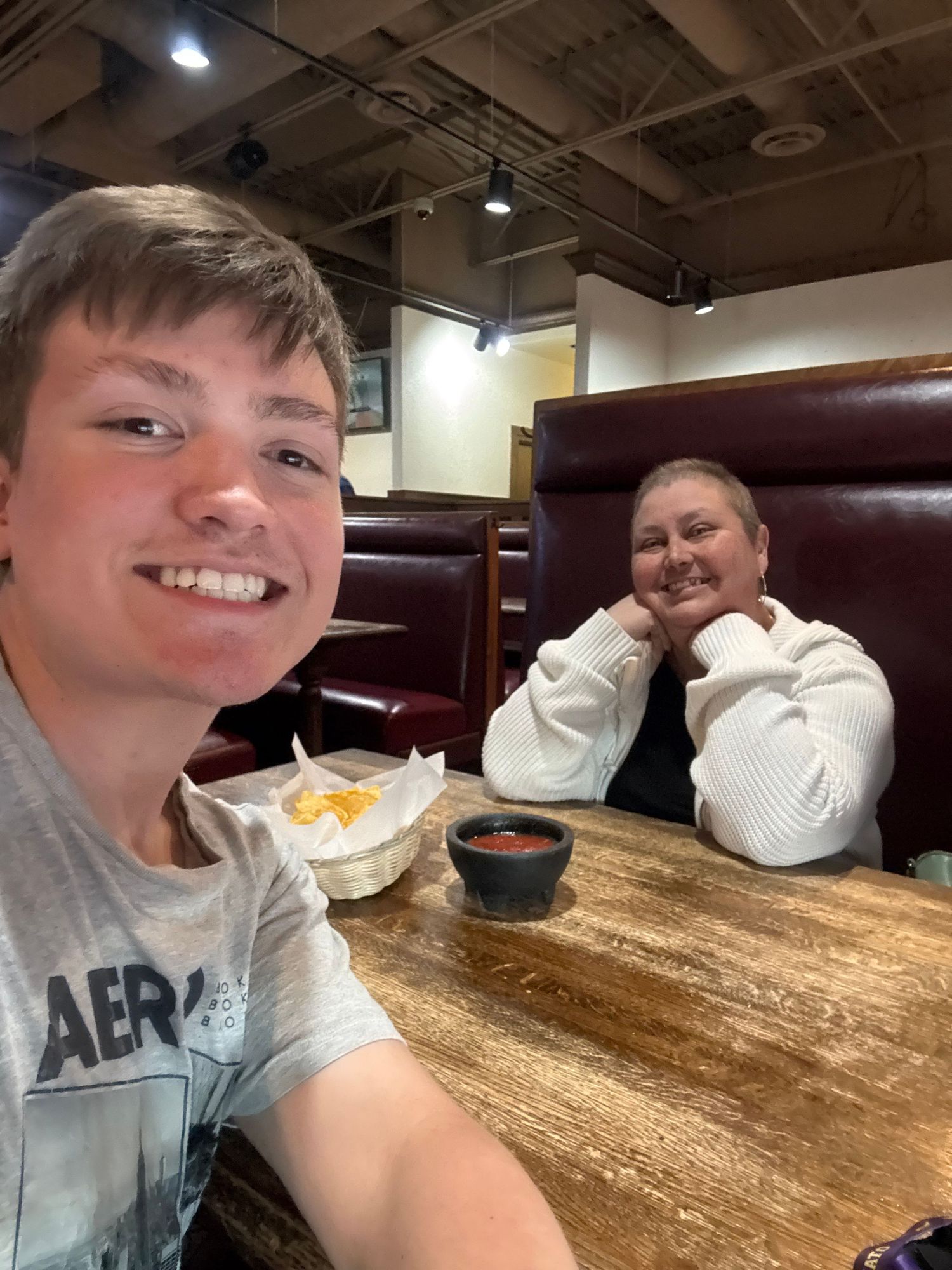 Two people smiling at a restaurant booth with chips and salsa on a wooden table.
