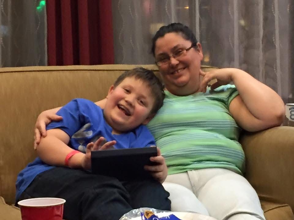 Young boy and woman smiling together on a couch while sharing a tablet device.