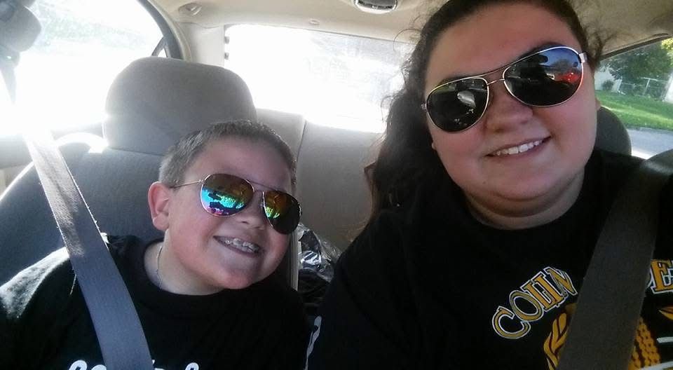 Two people wearing sunglasses smiling for a selfie inside a car on a sunny day.