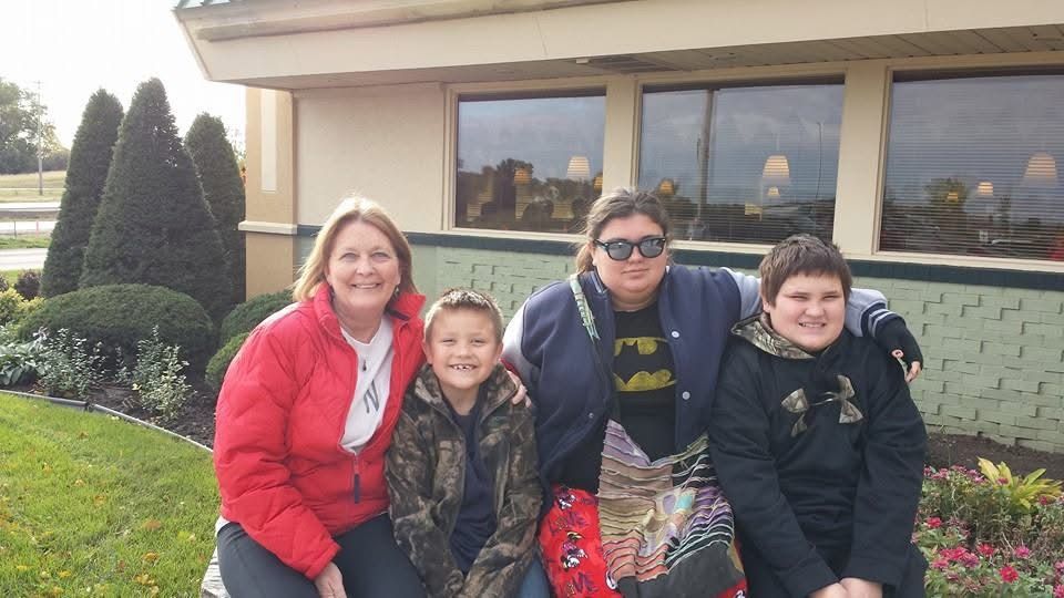 Family of four posing outdoors near a restaurant, including two boys and a woman in a red jacket on a cloudy day.