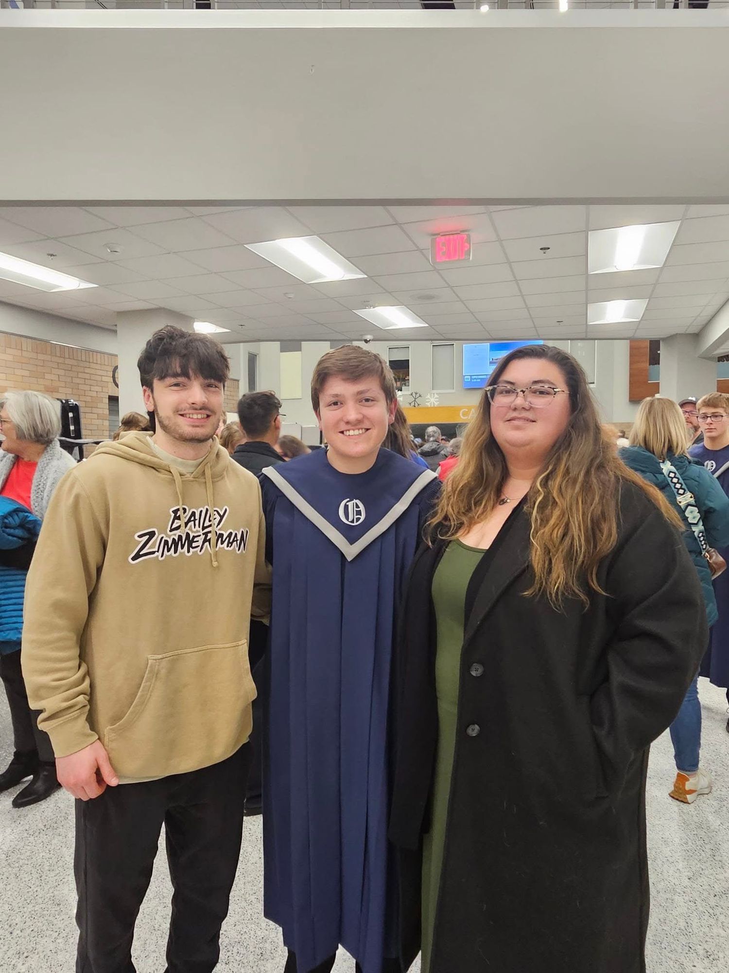 Three people posing together at a graduation ceremony, with the graduate wearing a navy blue cap and gown.