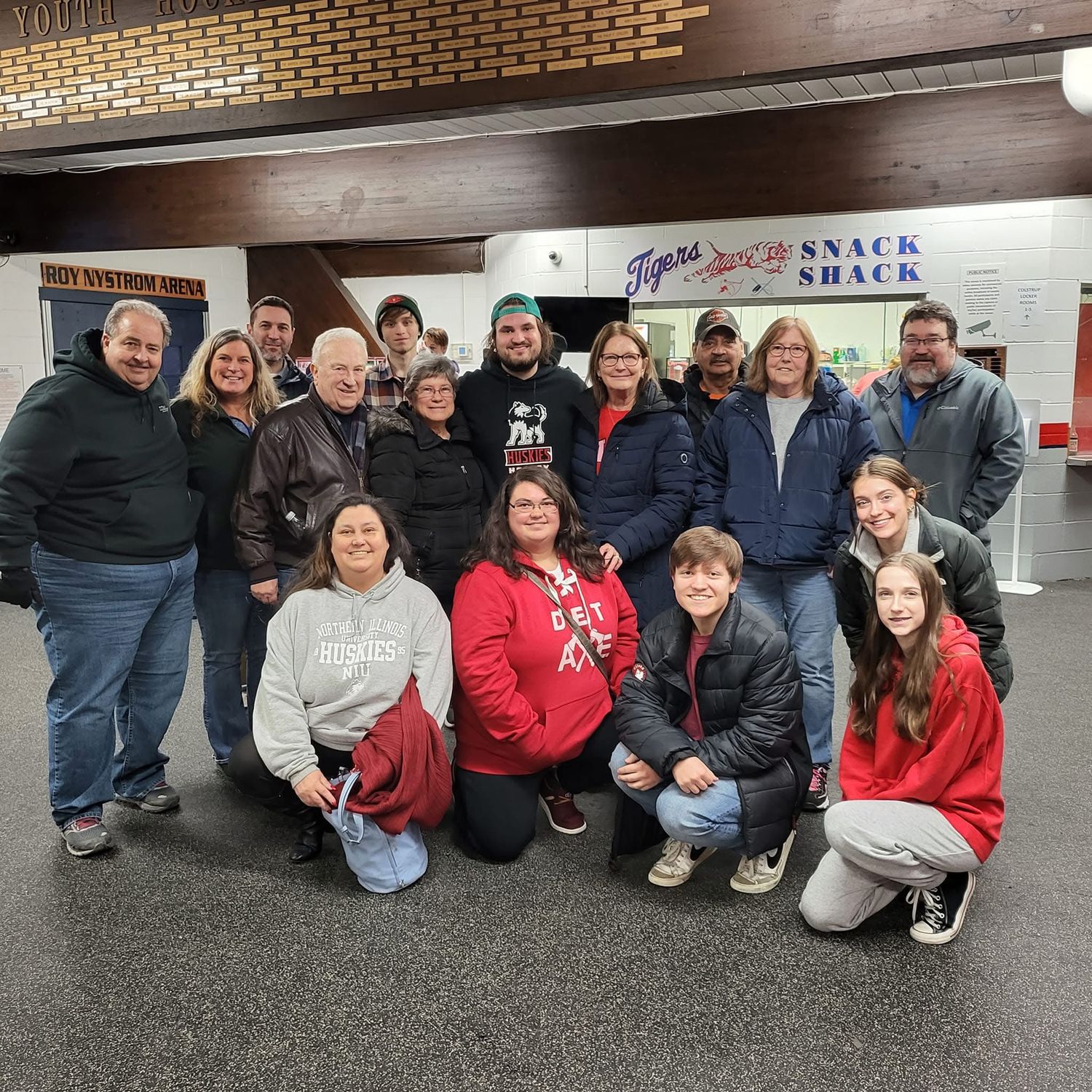 Large group of adults and teens posing together indoors near a Tigers Snack Shack concession stand.