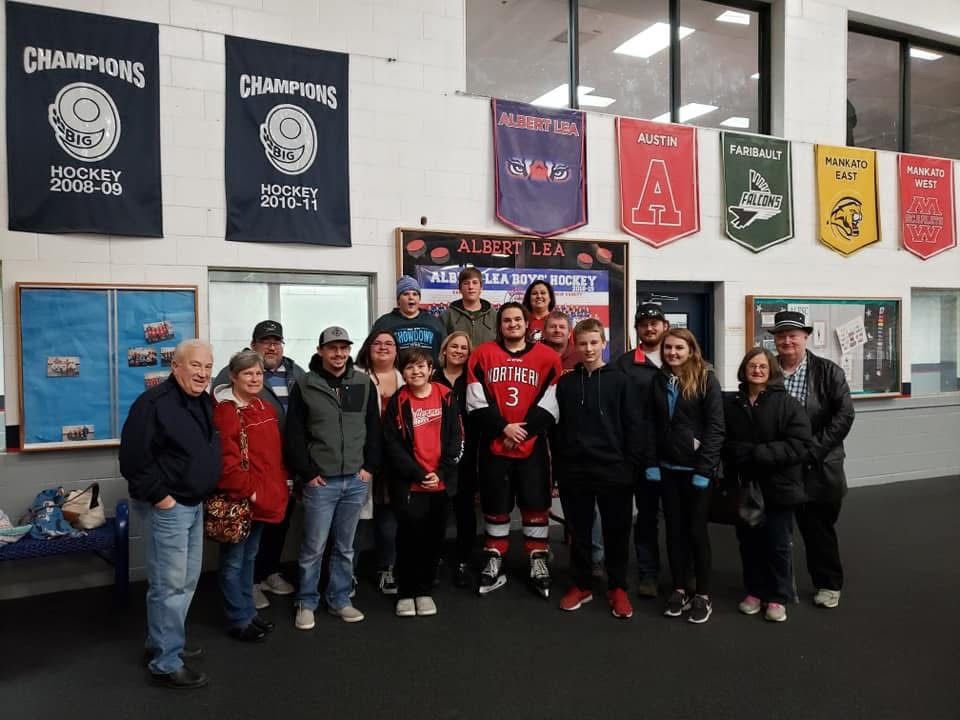 Group photo of hockey players and fans posing indoors near championship banners at an ice hockey rink facility.