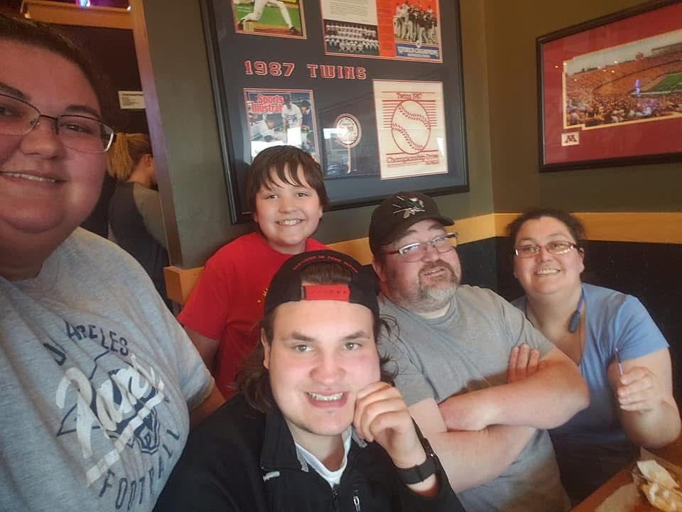 Group of five people smiling for a selfie in a sports-themed restaurant with Minnesota Twins memorabilia on the wall.
