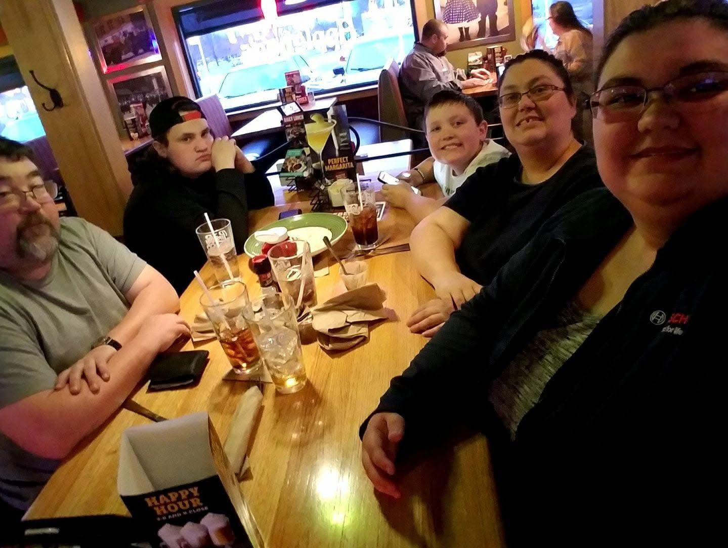 Group of five people smiling at a restaurant table with drinks during happy hour.