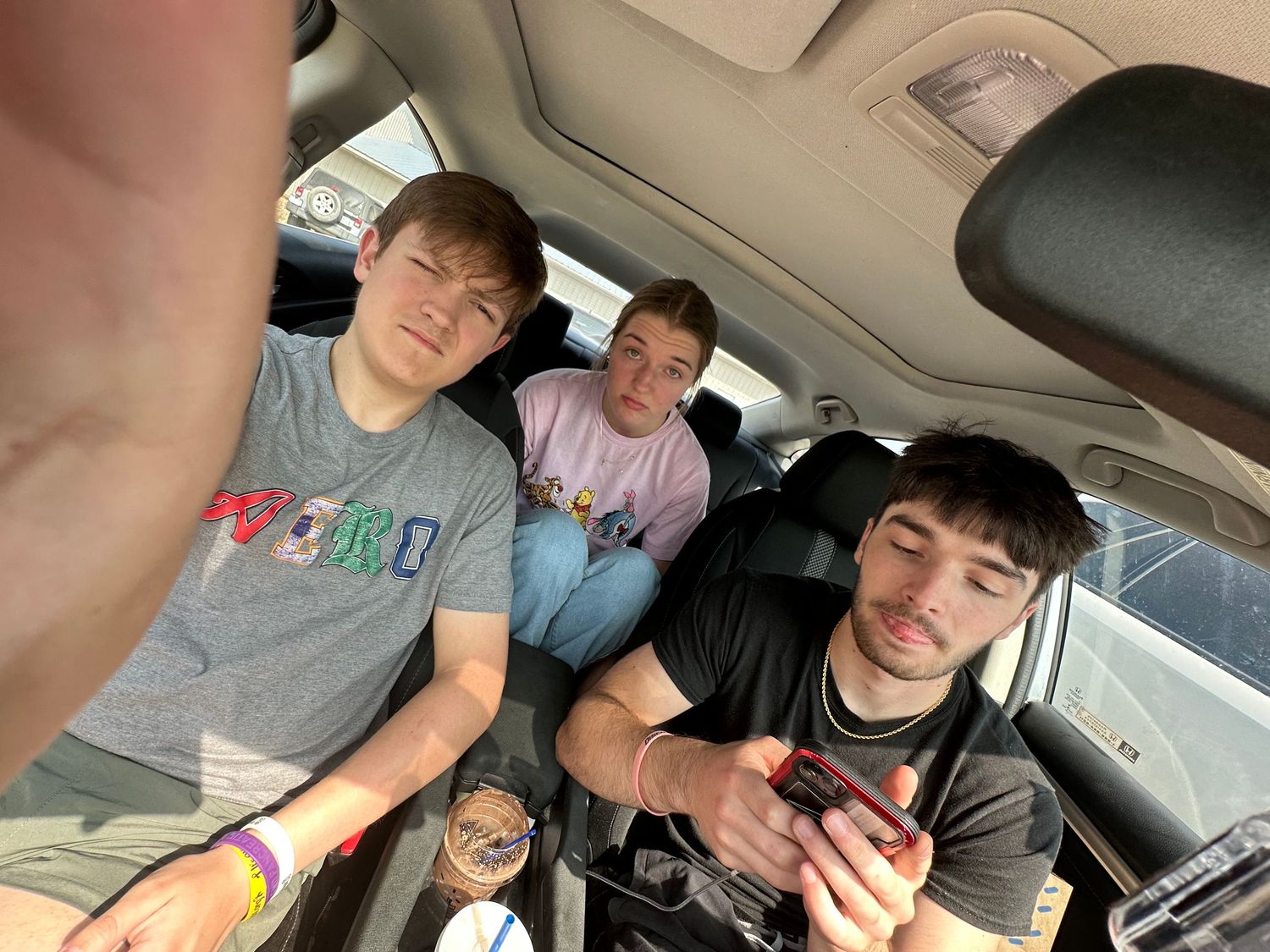 Three young men taking a selfie inside a car, smiling at the camera during a road trip.