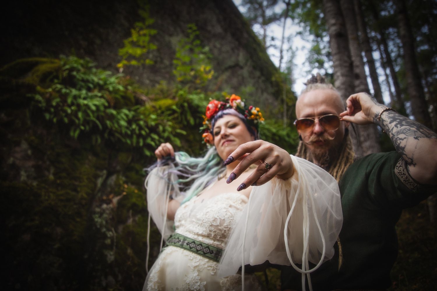 Bohemian bride with floral crown and tattooed groom in forest wedding ceremony outdoor nature setting.