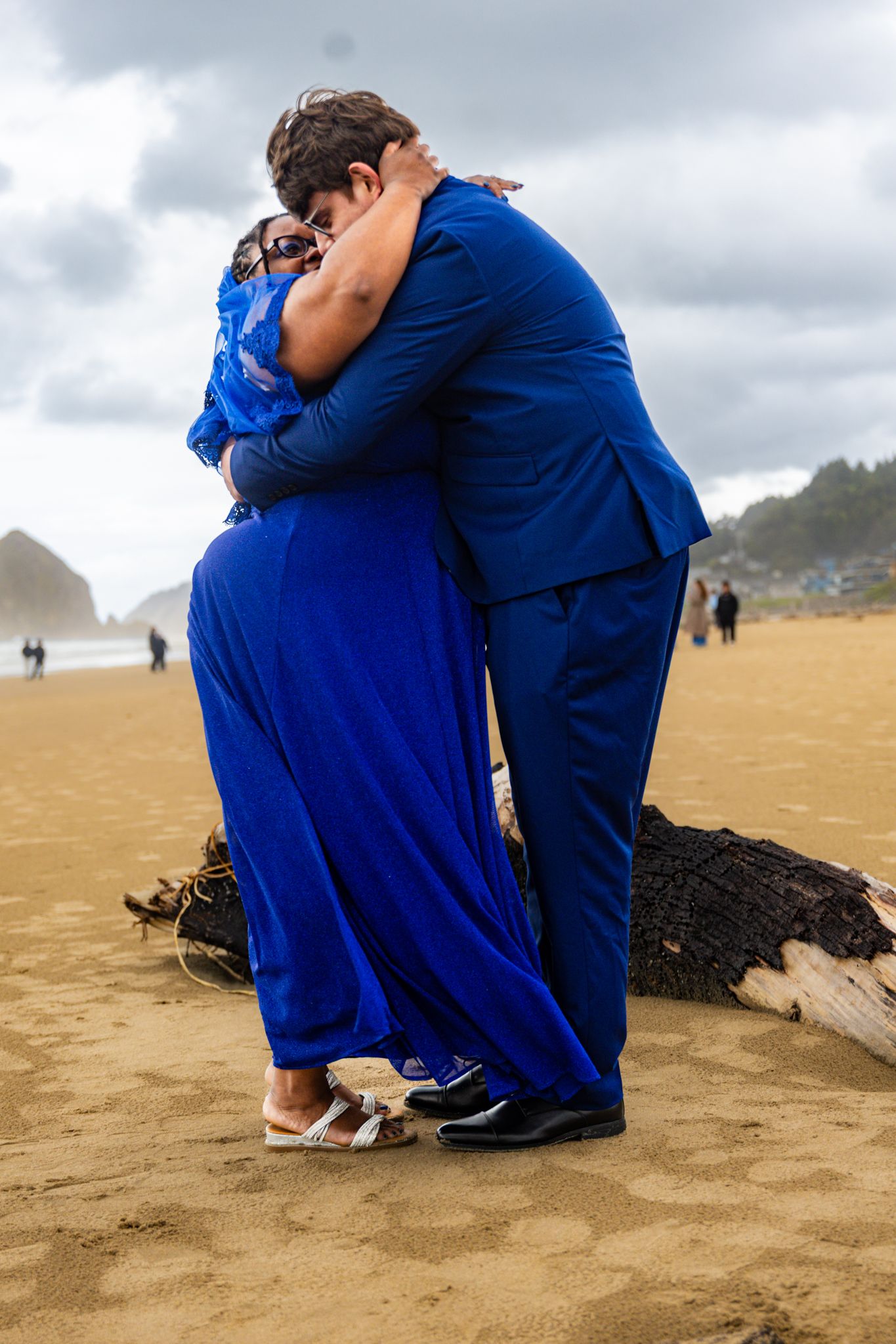 Newlyweds in royal blue outfits sharing a romantic hug on a sandy beach.