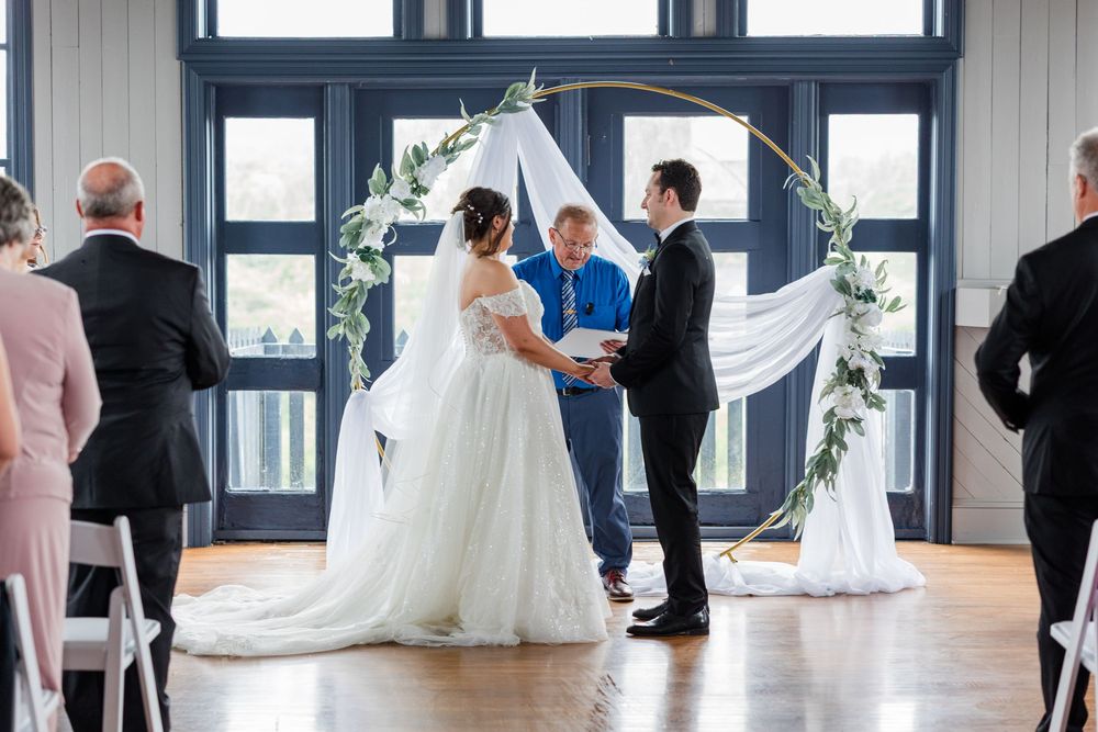 Bride and groom exchange vows under a circular floral arch at an elegant indoor wedding ceremony.