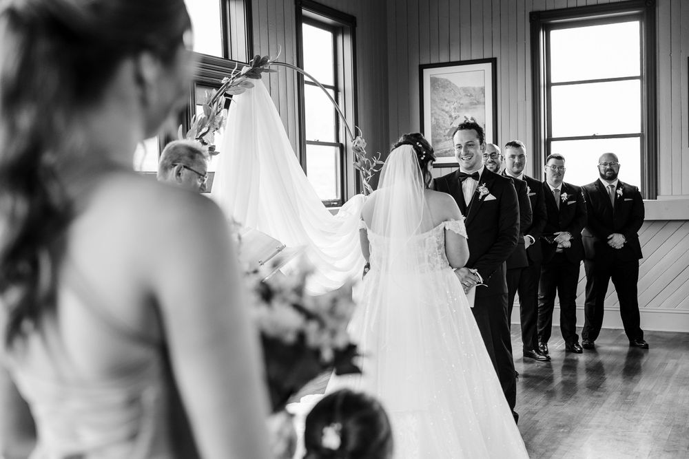 Black and white wedding ceremony photo showing bride and groom at altar with groomsmen standing in line at indoor venue.