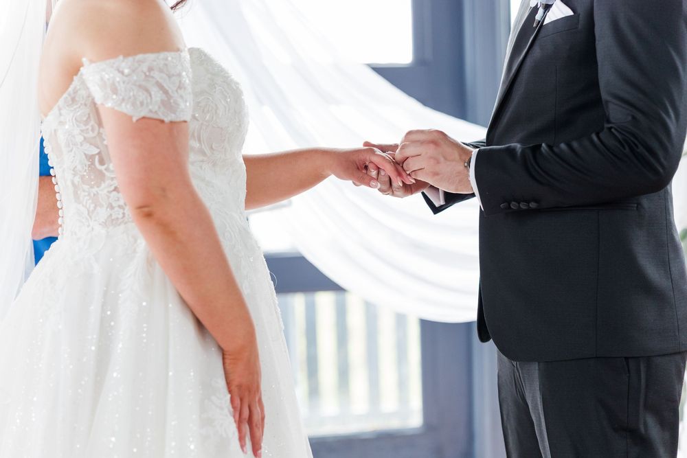 Bride and groom exchanging rings during wedding ceremony, bride in white lace gown, groom in black suit.