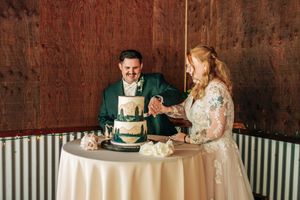Bride and groom cutting their green and gold wedding cake together at a rustic wood-paneled reception venue.