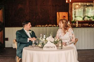 Bride and groom share a joyful moment at their sweetheart table decorated with white floral centerpiece.
