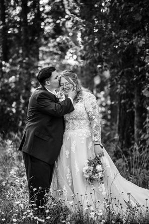 Black and white photo of bride and groom sharing a tender moment in a forest, bride holding a bouquet.