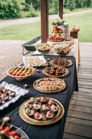 Elegant wedding appetizer buffet table with black cloth displaying assorted hors d\u0027oeuvres on gold platters.