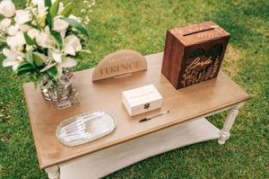 Elegant outdoor wedding guest book table with wooden signs, white florals, and decorative boxes on green grass.
