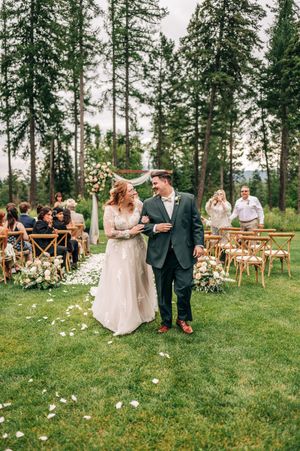 Newlyweds walk joyfully down the petal-lined aisle after their outdoor forest wedding ceremony.