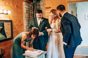 Wedding party signs marriage certificate at rustic wooden venue with bride in lace gown.
