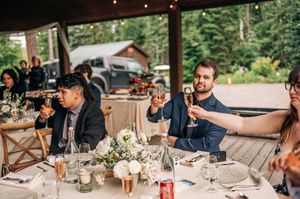 Wedding guests raising champagne glasses in a toast during an outdoor reception under a rustic pavilion.