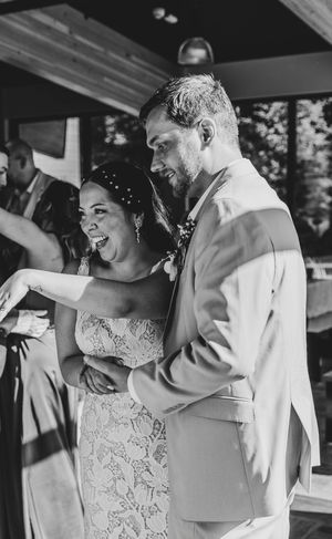 Black and white photo of a laughing bride in lace gown and groom in suit sharing a joyful moment at their wedding reception.
