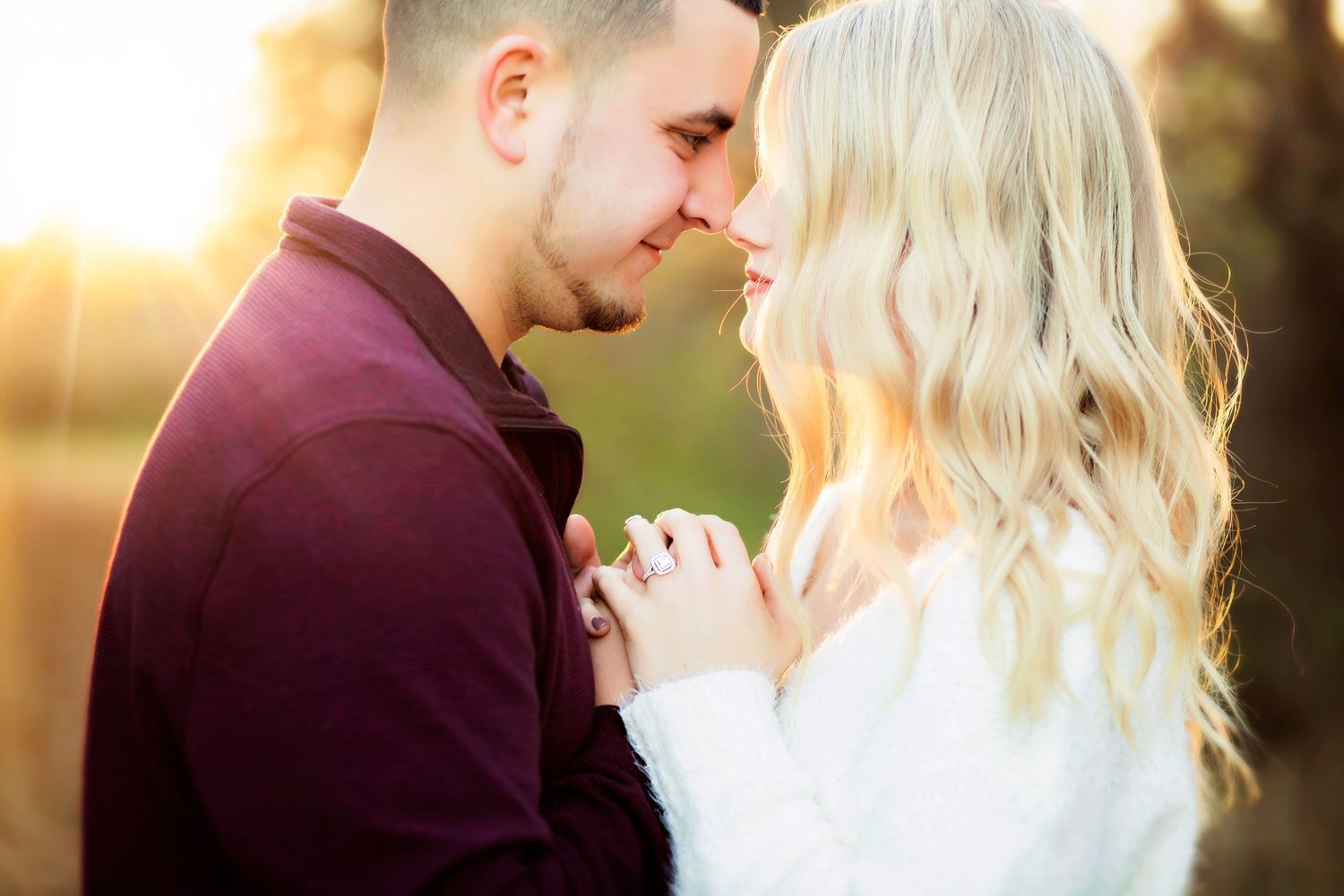 Couple sharing a romantic moment at golden hour, holding hands with an engagement ring visible.