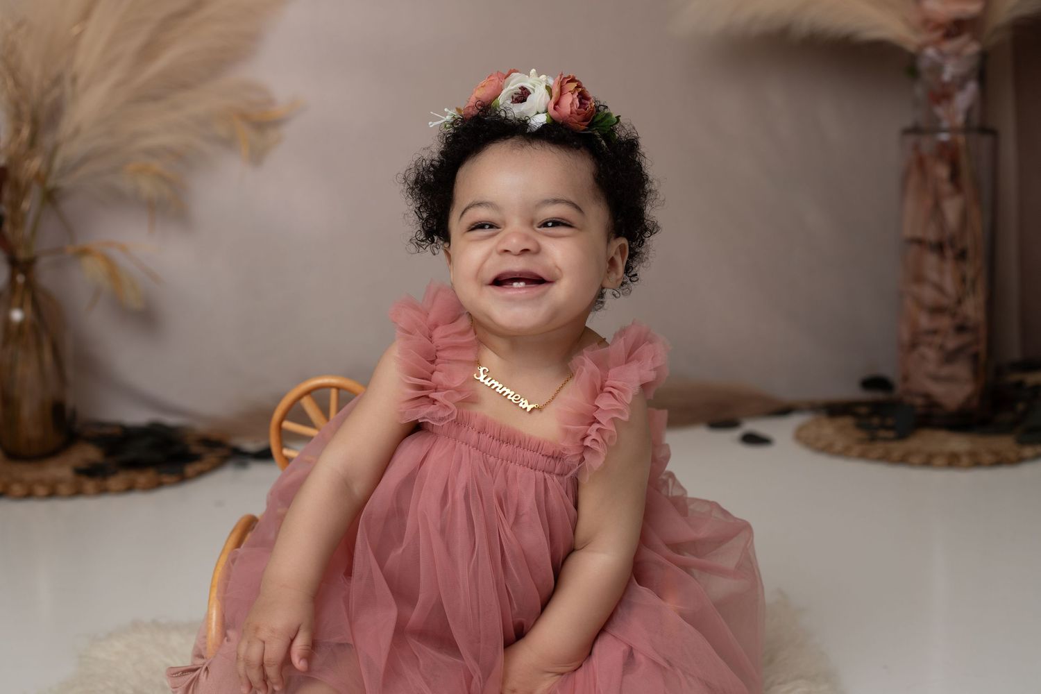 Smiling baby girl in pink tulle dress with floral crown during professional photo session.