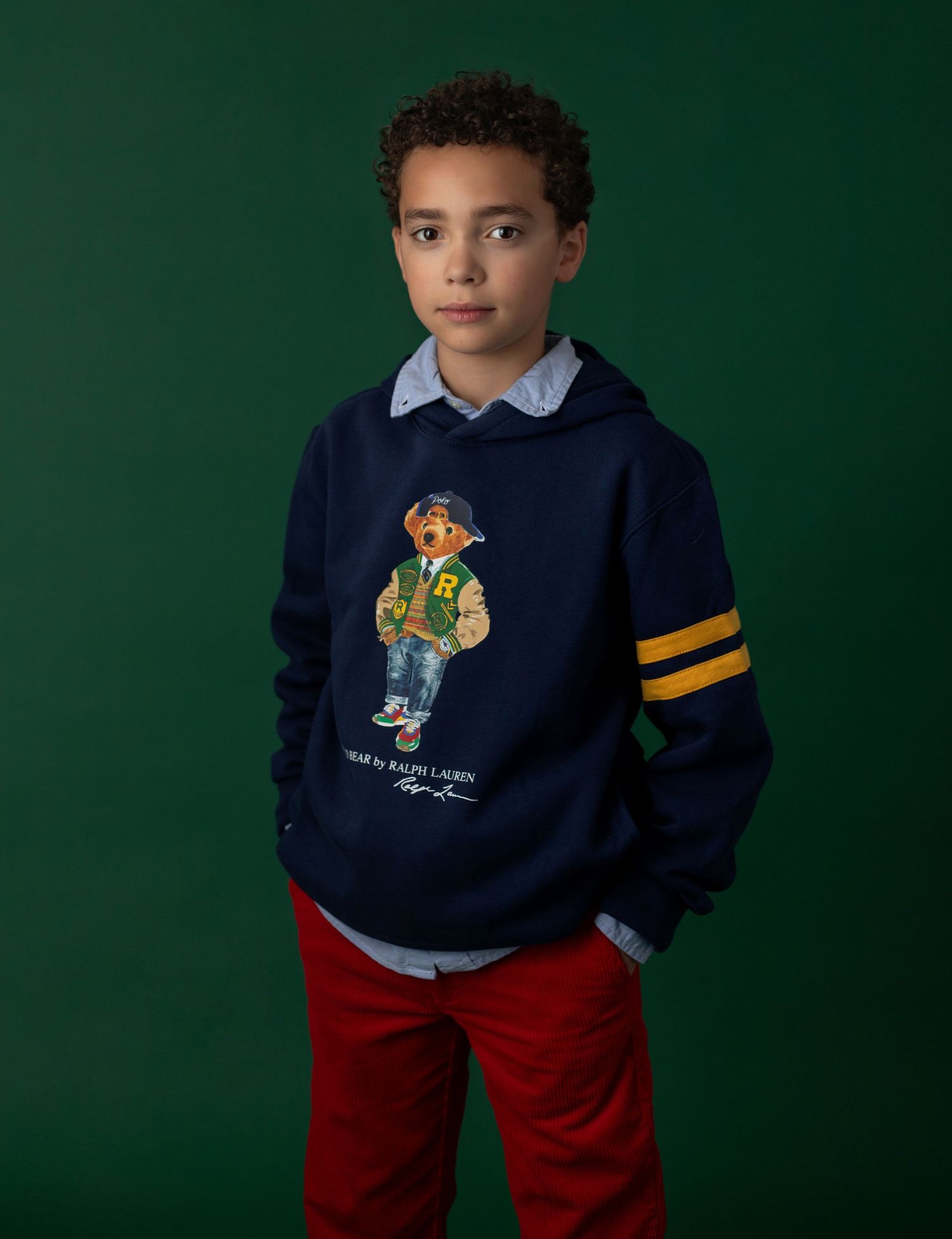 Boy wearing a navy Ralph Lauren Polo Bear hoodie with yellow stripes, layered over a blue shirt with red pants.