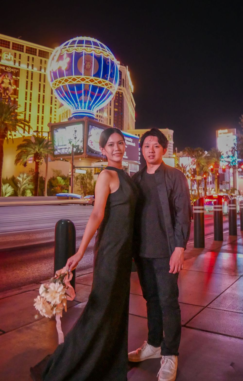 Couple posing on the Las Vegas Strip at night with illuminated Paris Hotel hot air balloon in the background.