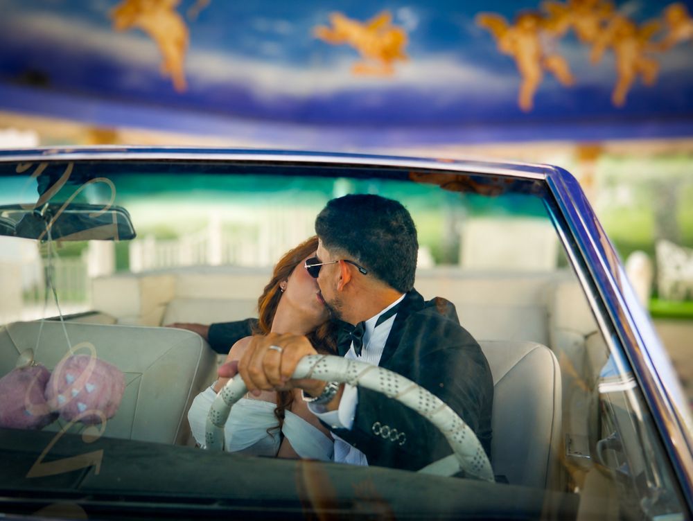Newlyweds sharing a romantic kiss inside a vintage convertible car with angel-painted ceiling at Las Vegas chapel.