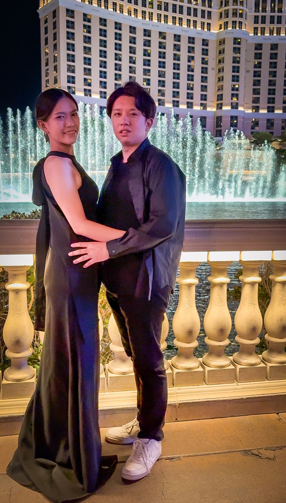 Couple in elegant black attire posing in front of the Bellagio fountain at night in Las Vegas.