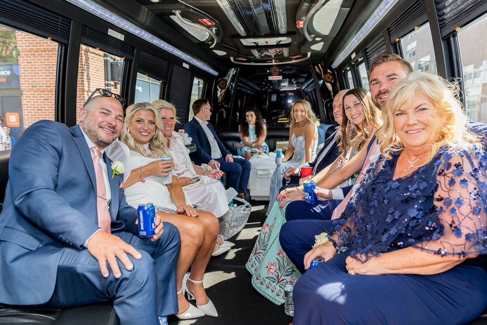 Wedding party celebrating inside a party bus, dressed in formal attire, smiling and enjoying drinks together.