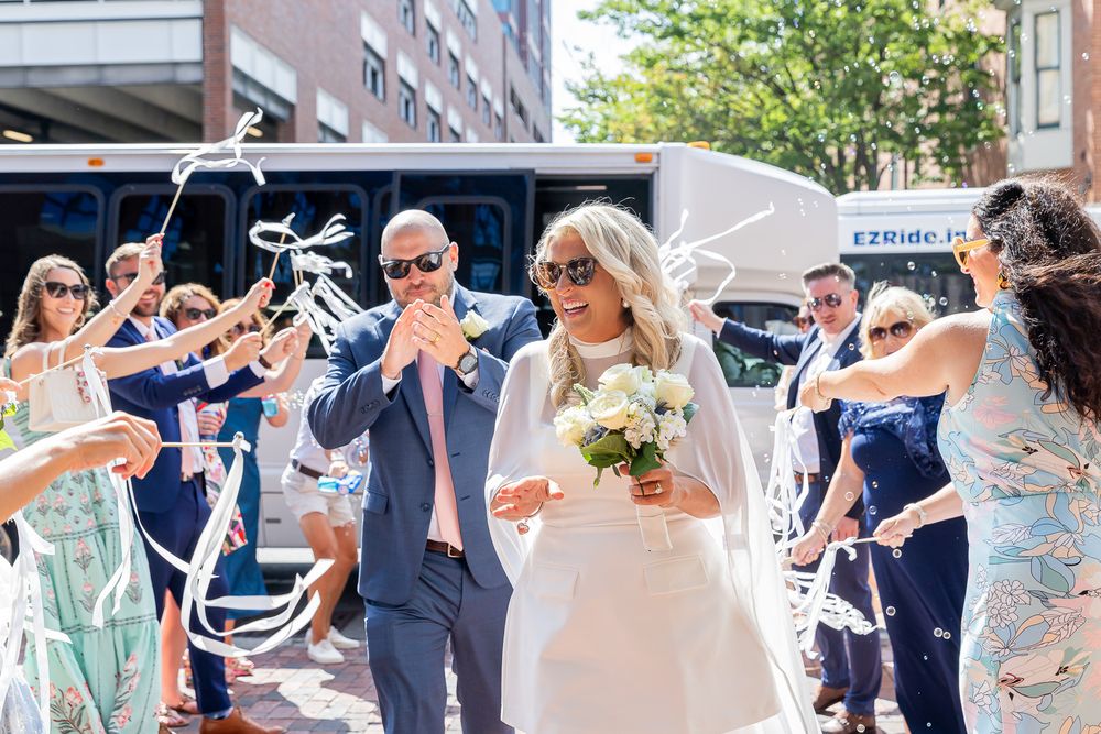 Bride and groom walk through cheering guests tossing streamers outside an EZRide bus on their wedding day.