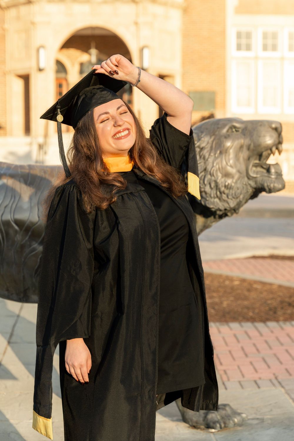 Towson University grad student standing in front of a Tiger statue wearing her regalia