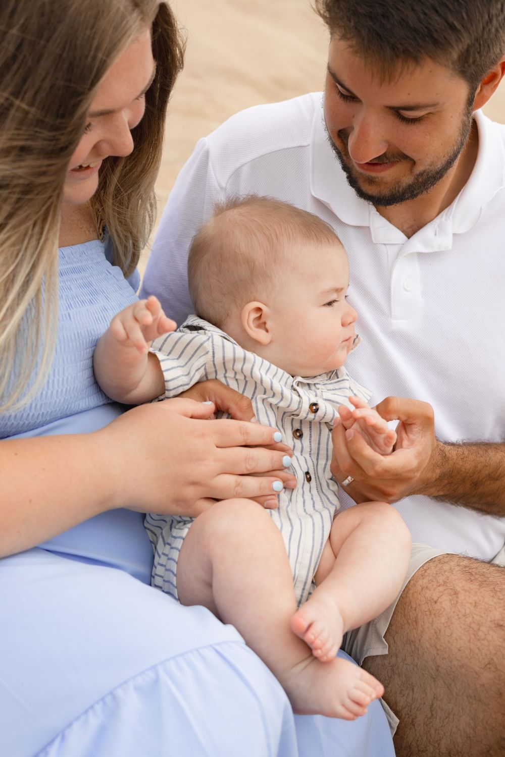 Happy young family with mother and father smiling at their baby boy sitting outdoors on a sunny day.