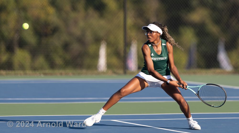 Tennis player in green uniform stretches for a return shot on blue court.