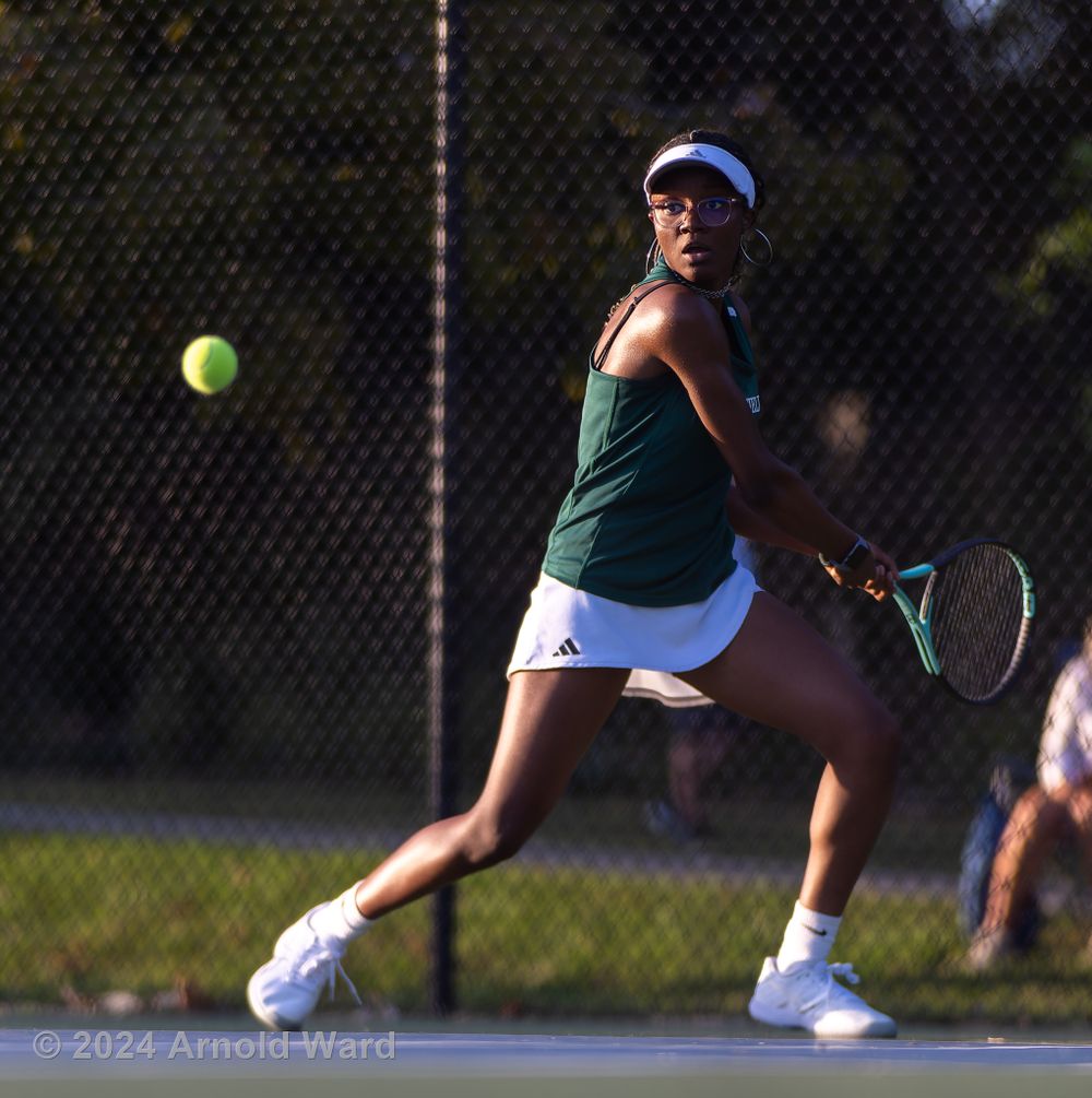 Tennis player wearing green and white uniform makes athletic motion during match on outdoor court.